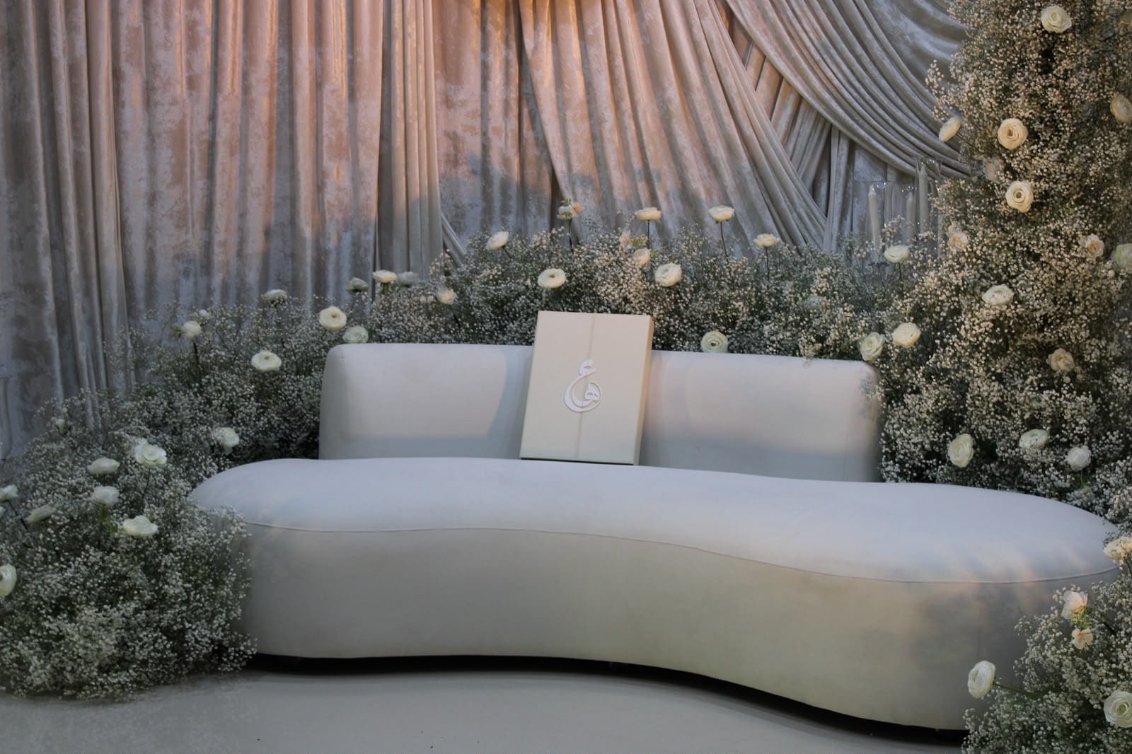 Curved ivory sofa framed by baby's breath and white roses